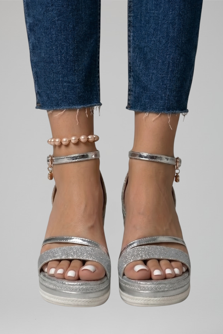 Silver glittery cushioned sandals on feet, paired with blue denim jeans in a studio setting.