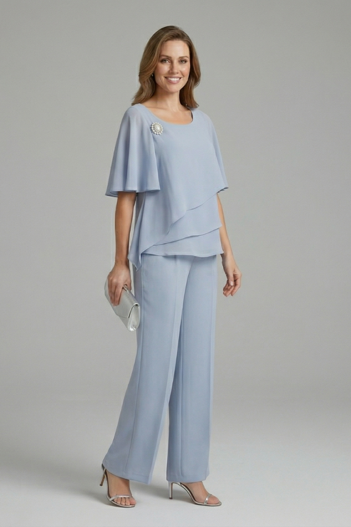 Model showcasing light blue layered top and trousers set from the back, holding a clutch, in studio.