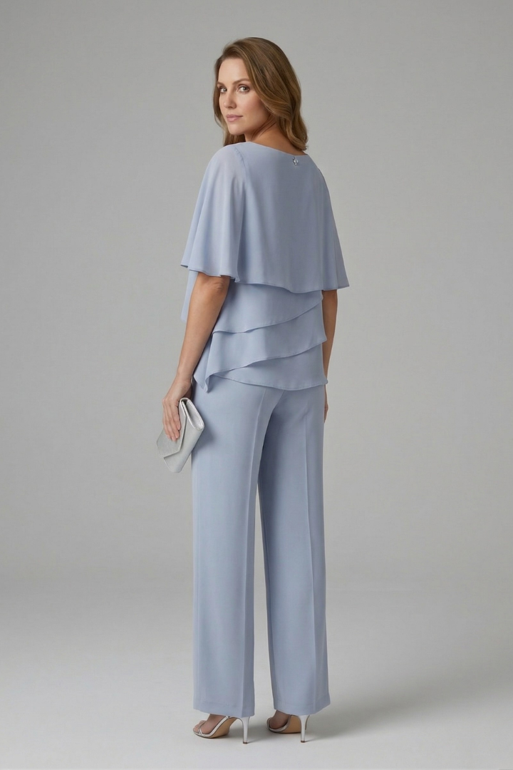 Model wearing dark blue layered top and trousers set, holding a clutch, in a studio setting.