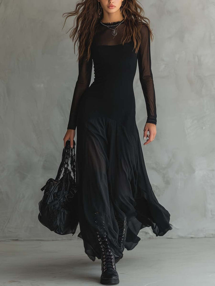 Woman in a black flowy dress and boots walking in a studio with a textured grey wall, carrying a stylish black bag.
