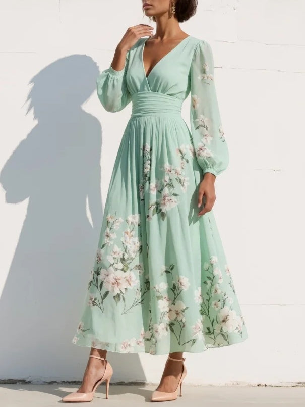 Woman wearing a light green midi dress with floral design, long sleeves, posing in sunlight against a white wall.