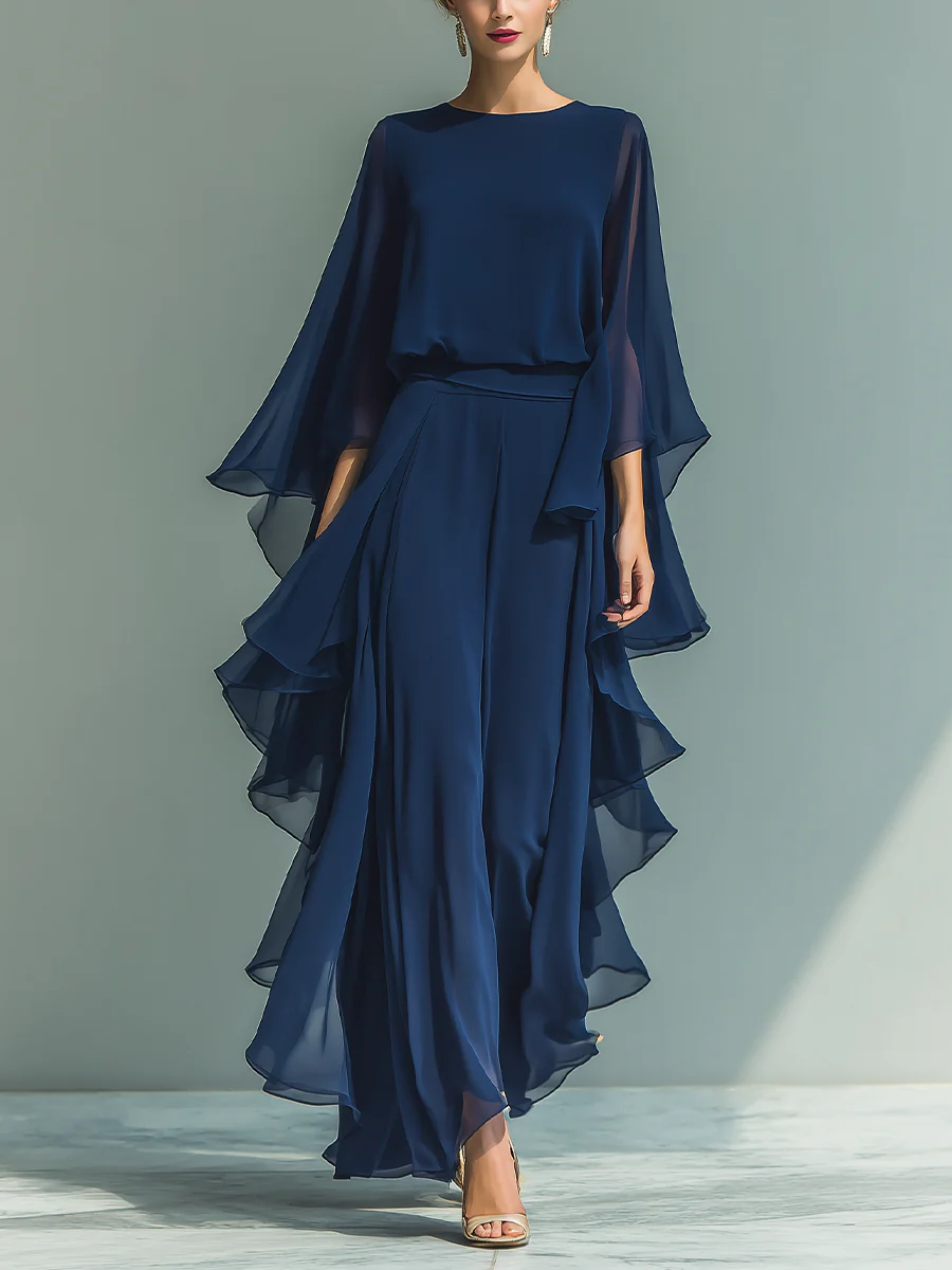 Elegant deep blue two-piece set with flowing layers and cape sleeves, worn with heels in a plain studio setting.