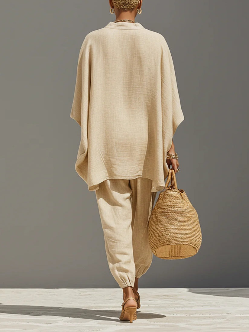 Rear view of beige set featuring a flowy top and tapered pants, accessorized with a woven bag, on a plain background.