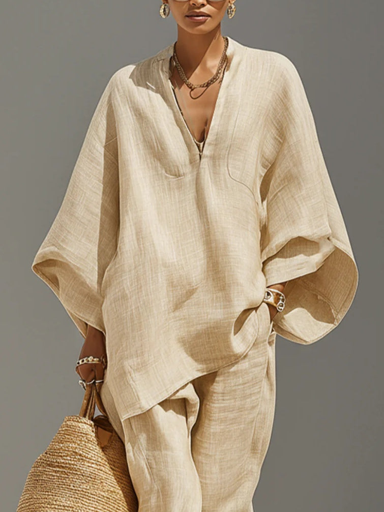 Front view of beige set with loose top and pants, featuring a woven bag and jewelry, against a neutral background.