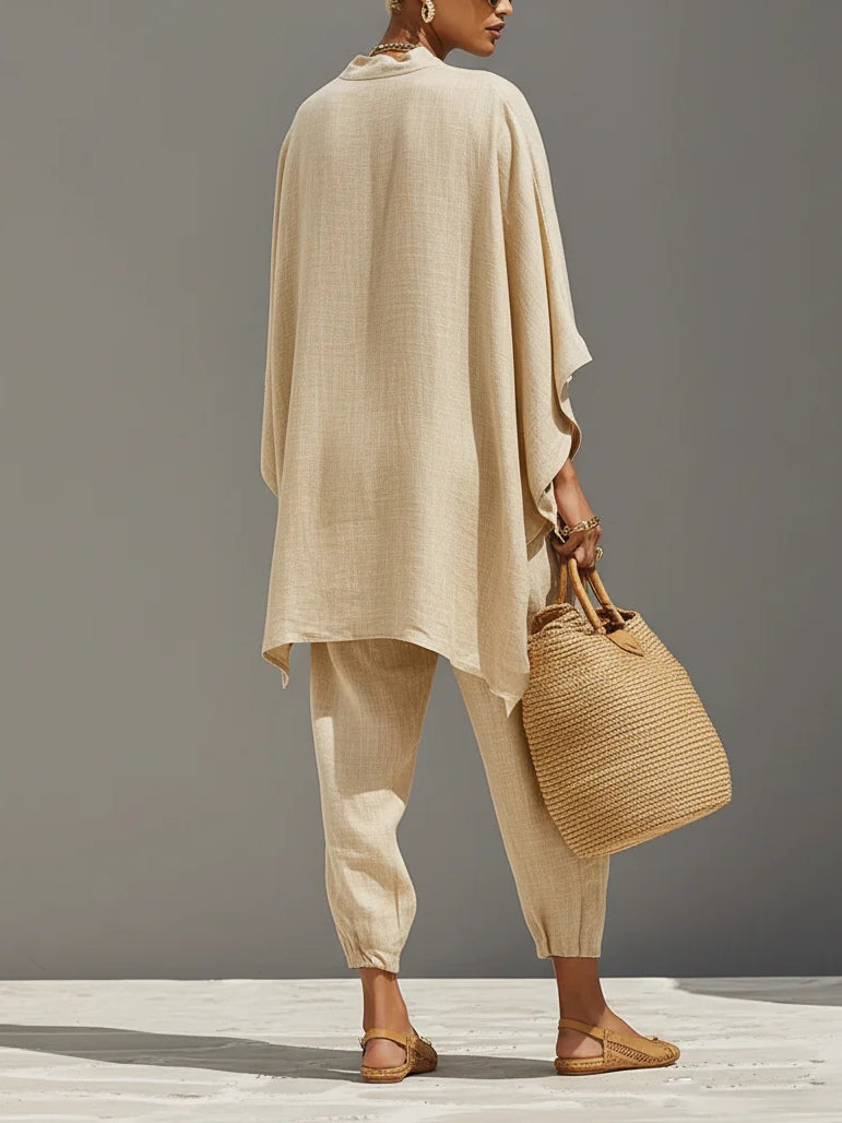 Back view of beige set with flowing top and tapered pants, holding a woven bag, against a neutral backdrop.