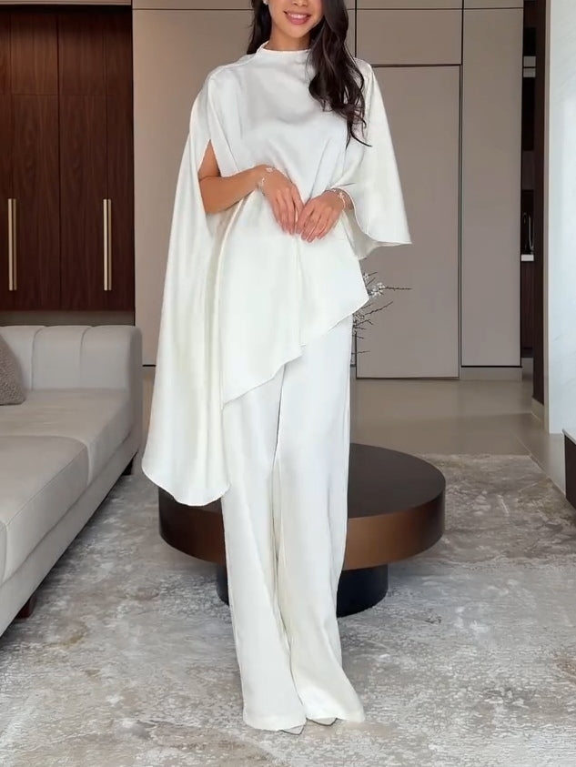 Woman in white flowing two-piece set standing in a modern living room with wood accents and neutral decor.