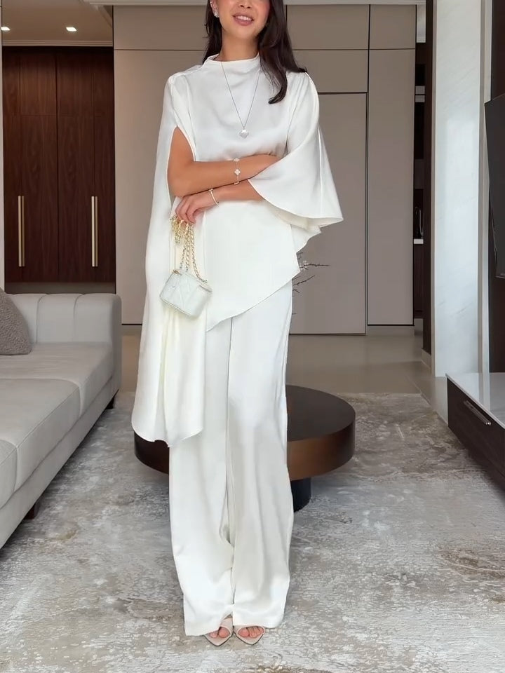 Woman in white two-piece set holding a small handbag, standing confidently in a chic living space.