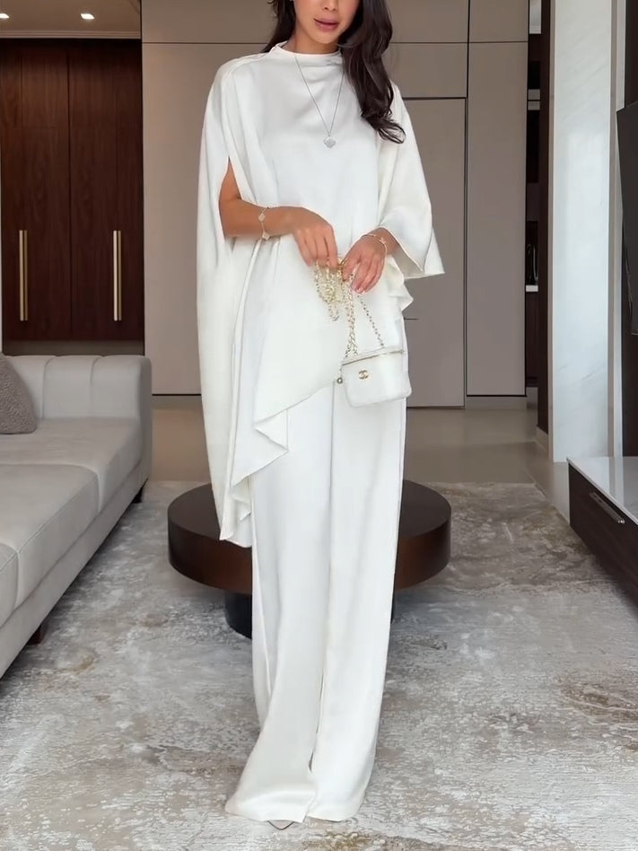 Woman wearing a white two-piece set holding a small white handbag in a stylish living room setting.