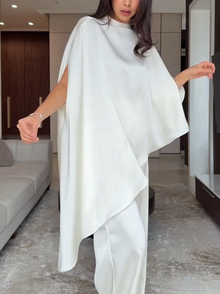 Woman in flowing white two-piece set posing with arms outstretched in an elegant living room.