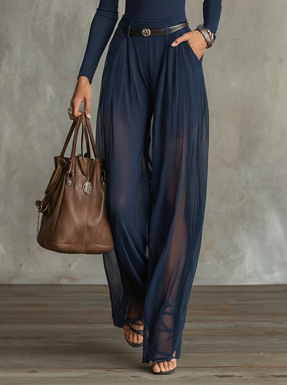 Navy blue sheer wide-leg pants with a brown leather handbag, worn in a sophisticated studio environment.