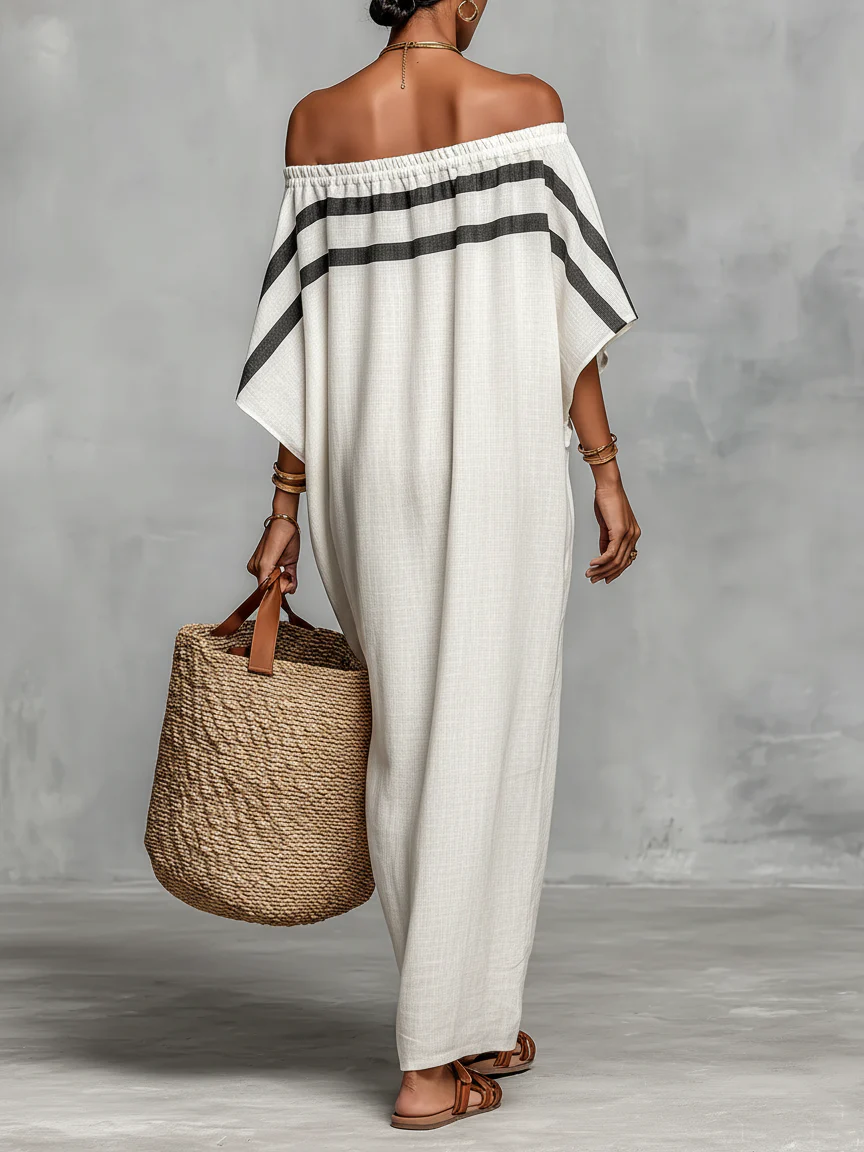 Back view of an off-shoulder white maxi dress with black stripes, accessorized with a woven tote in a studio setting.