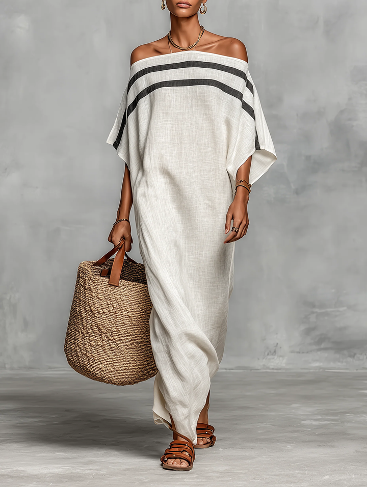 Elegant off-shoulder white maxi dress with black stripes, paired with a woven tote and sandals in a studio setting.