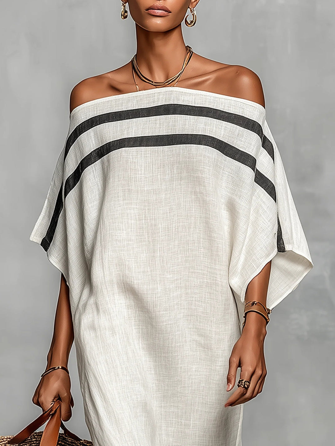 Close-up of an elegant off-shoulder white maxi dress with black stripes, accessorized with gold jewelry in a studio setting.