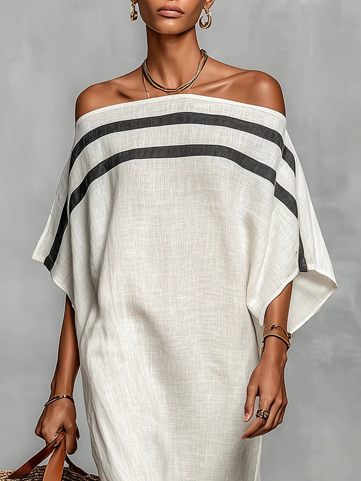 Close-up of an elegant off-shoulder white maxi dress with black stripes, accessorized with gold jewelry in a studio setting.