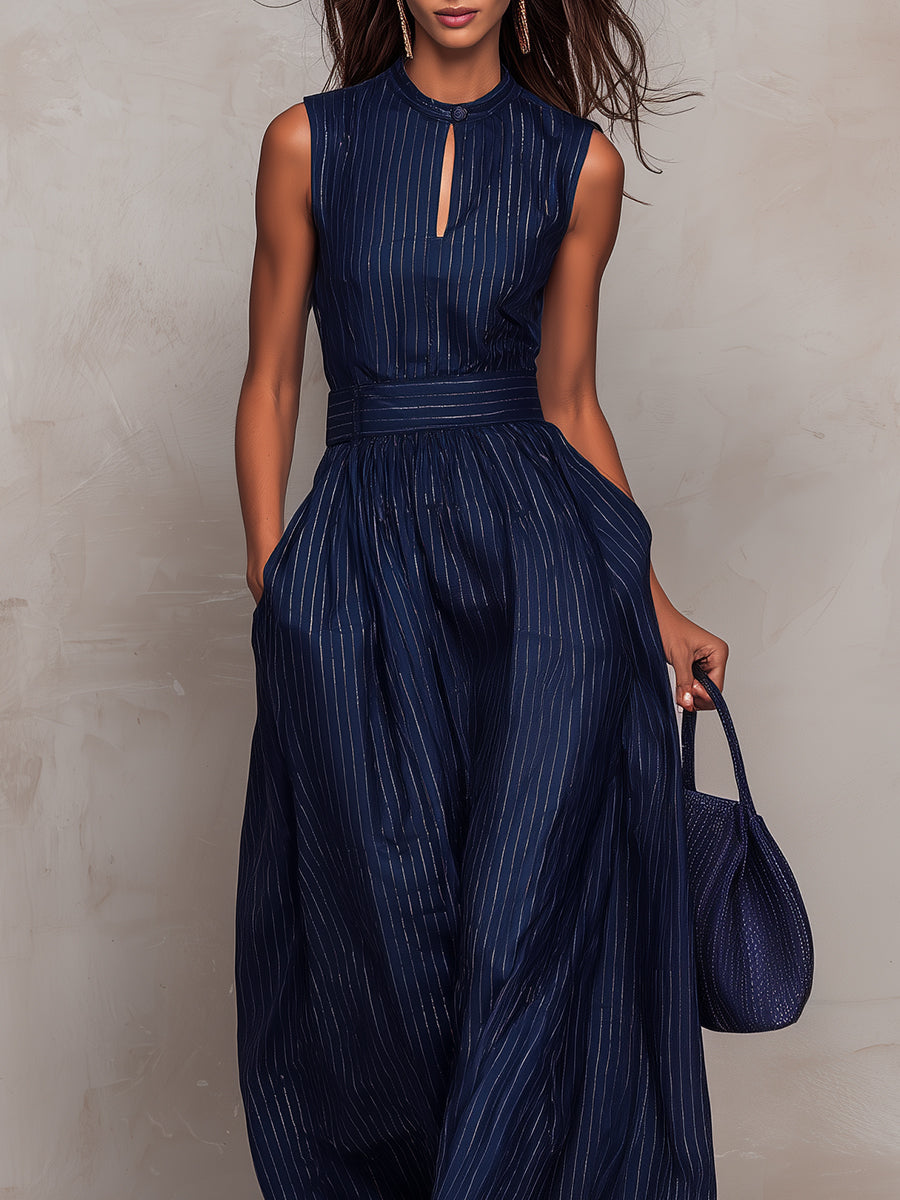 Close-up of a model wearing a navy wide-leg jumpsuit with vertical stripes, holding a matching bag, against a beige backdrop.