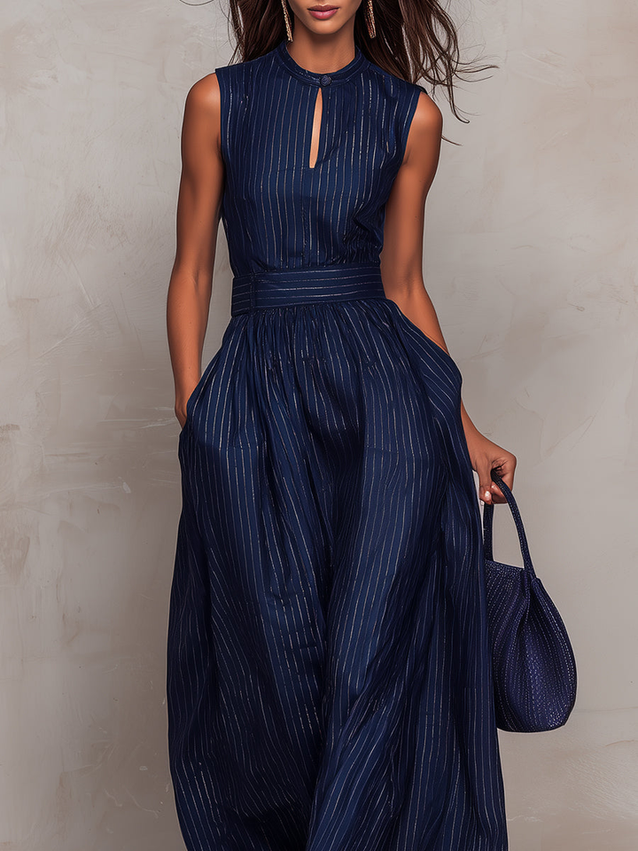 Close-up of a model wearing a navy wide-leg jumpsuit with vertical stripes, holding a matching bag, against a beige backdrop.