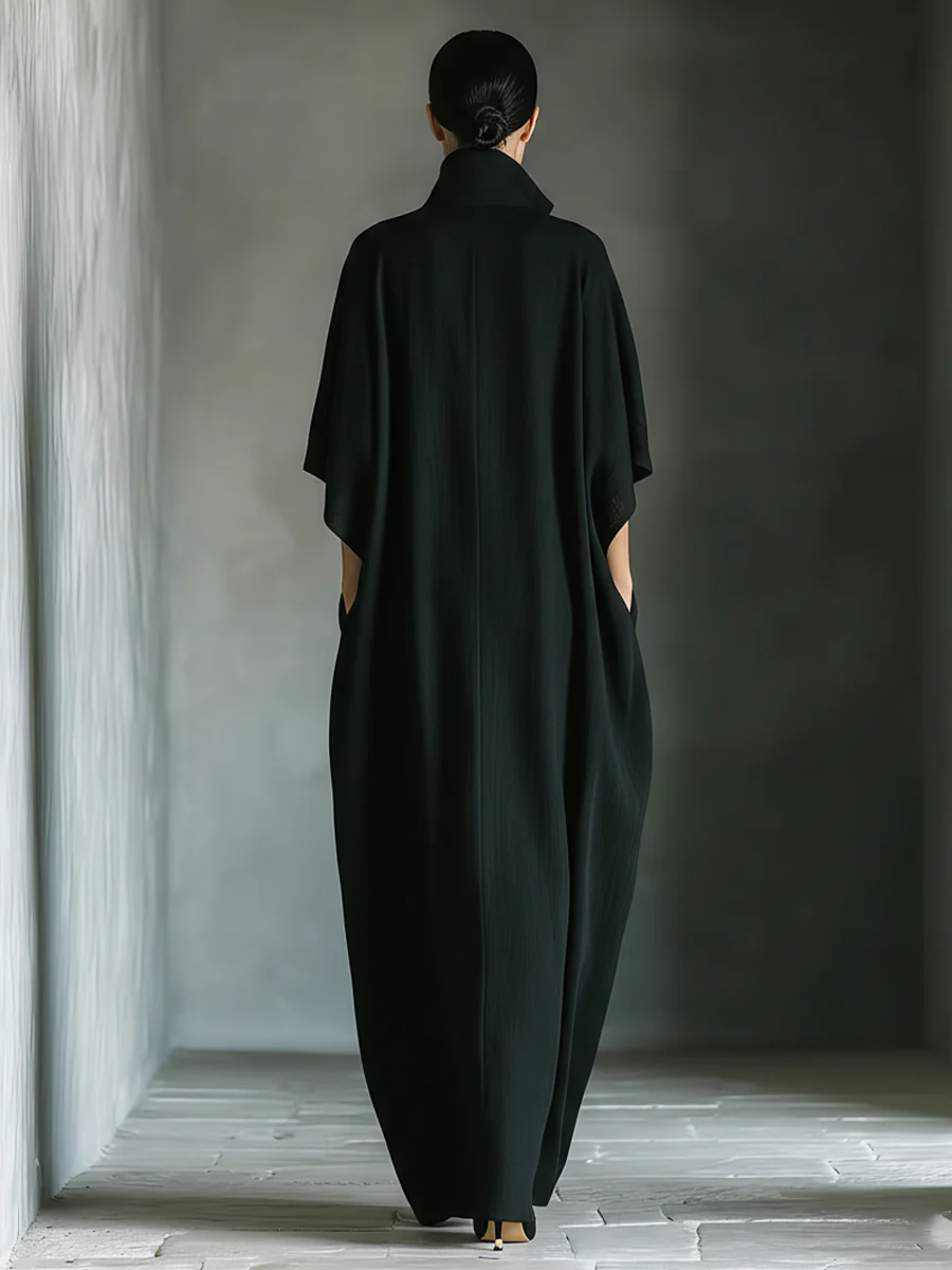 Back view of a black maxi dress with high collar worn by a person in a minimalist indoor setting.