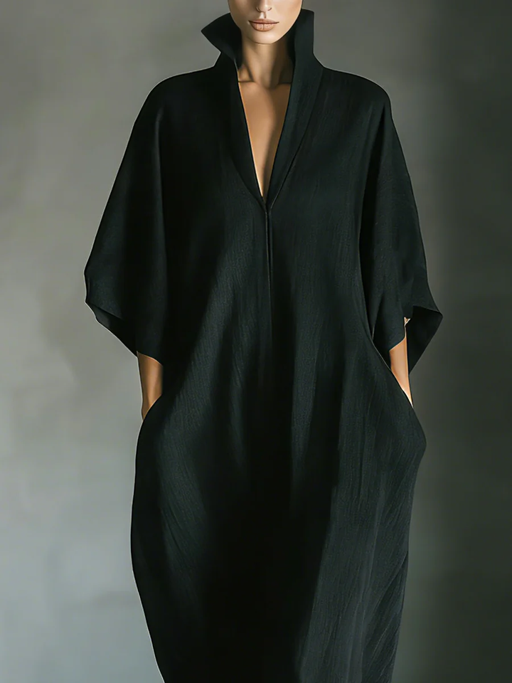 Close-up of a flowing black maxi dress with high collar worn by a person, set in a minimalist indoor space.