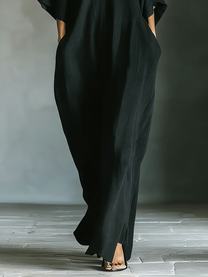 Bottom half of a black maxi dress with subtle slit, worn by a person in a minimalist indoor setting.