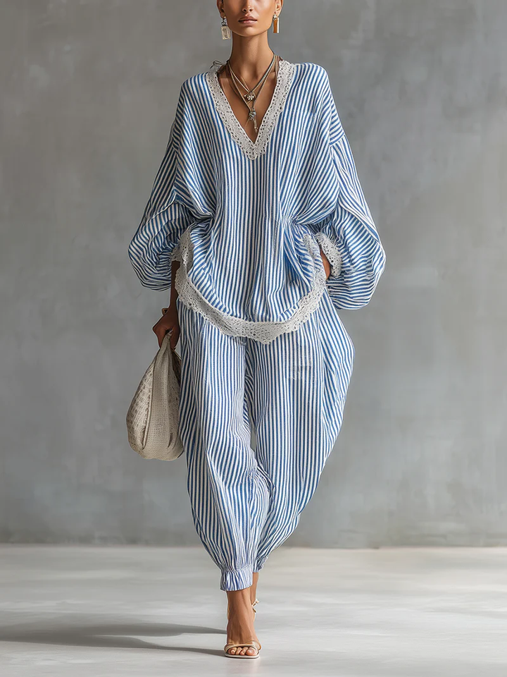 Model wearing a blue and white striped two-piece set with lace trim, holding a woven bag, against a gray studio background.