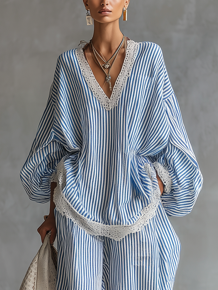 Close-up of blue and white striped top with lace trim, styled with layered necklaces, in a gray studio background.