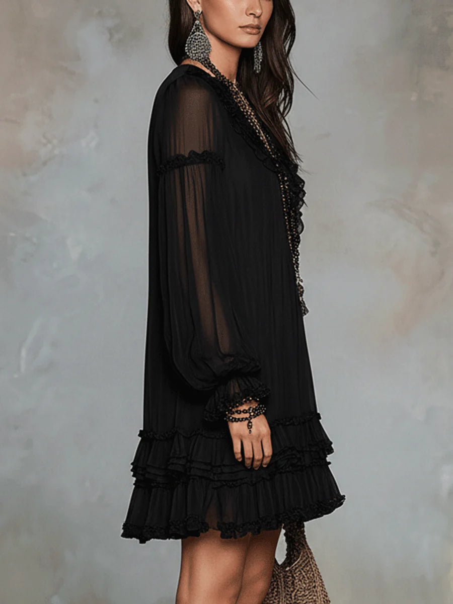 Side profile of black mini dress with ruffled layers and sheer long sleeves, in a studio backdrop.