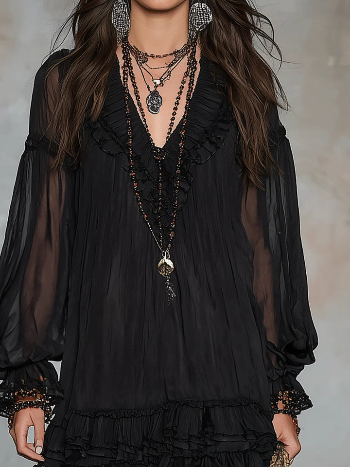 Close-up of black mini dress with ruffled details and layered necklaces, studio background.