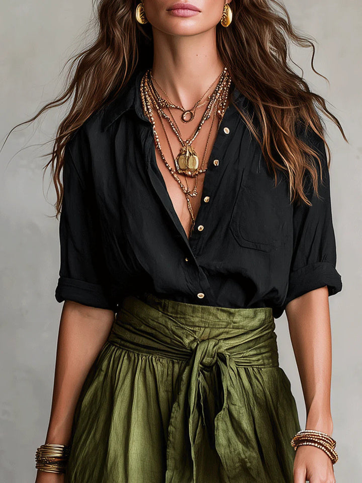 Close-up of a woman wearing a Vita Two-Piece Set with a black top, layered necklaces, and green skirt. Neutral background.