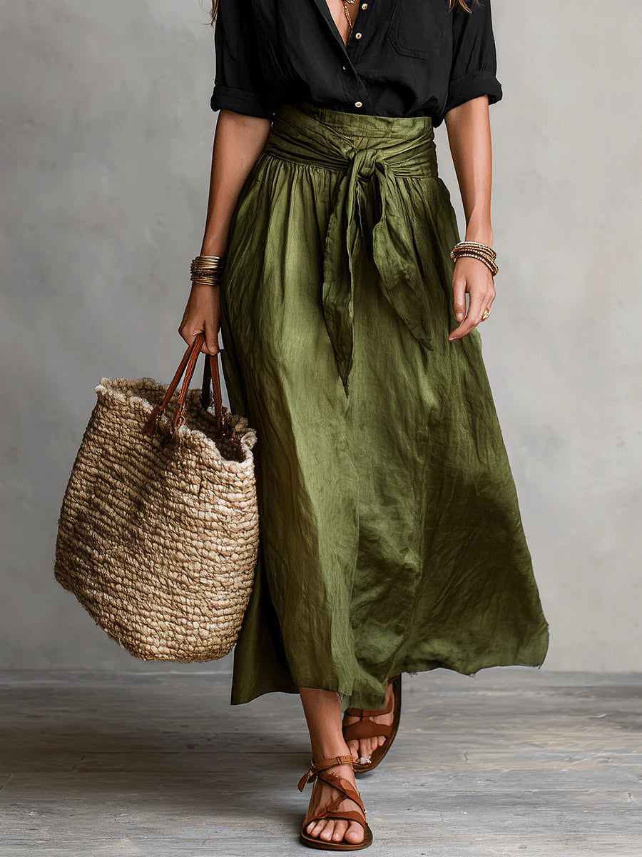 Front view of a woman in a Vita Two-Piece Set, black top and green skirt, holding a woven tote. Neutral studio background.