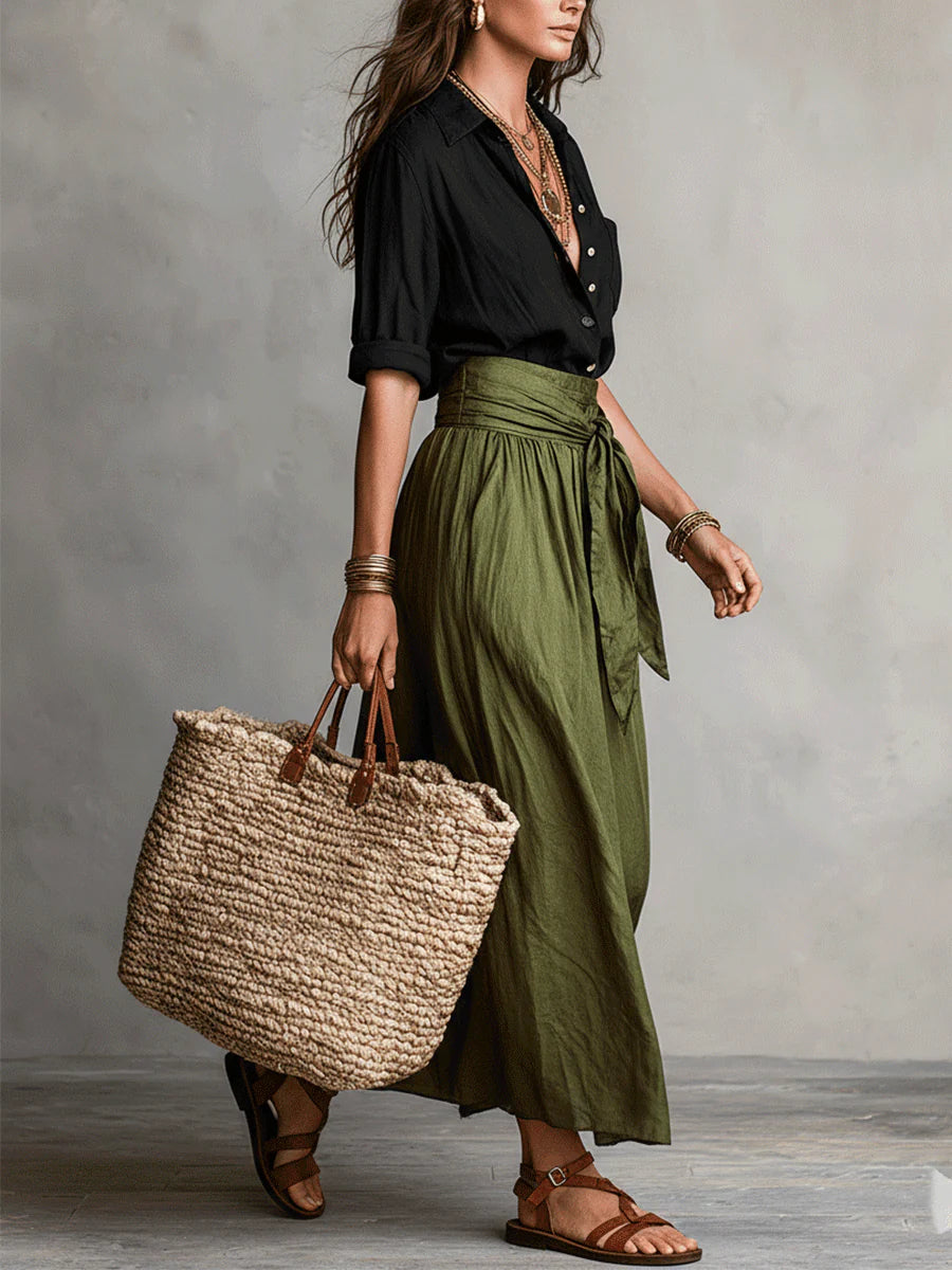 Side view of a woman in a Vita Two-Piece Set with black top, green skirt, and woven tote bag. Neutral studio background.