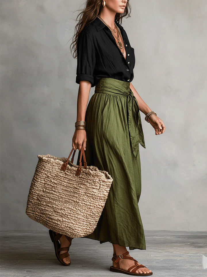 Side view of a woman in a Vita Two-Piece Set with black top, green skirt, and woven tote bag. Neutral studio background.
