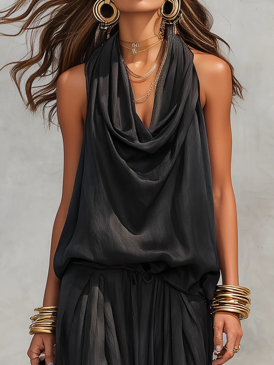 Close-up of woman wearing black two-piece set with draped neckline, large earrings, and bangles, neutral backdrop.