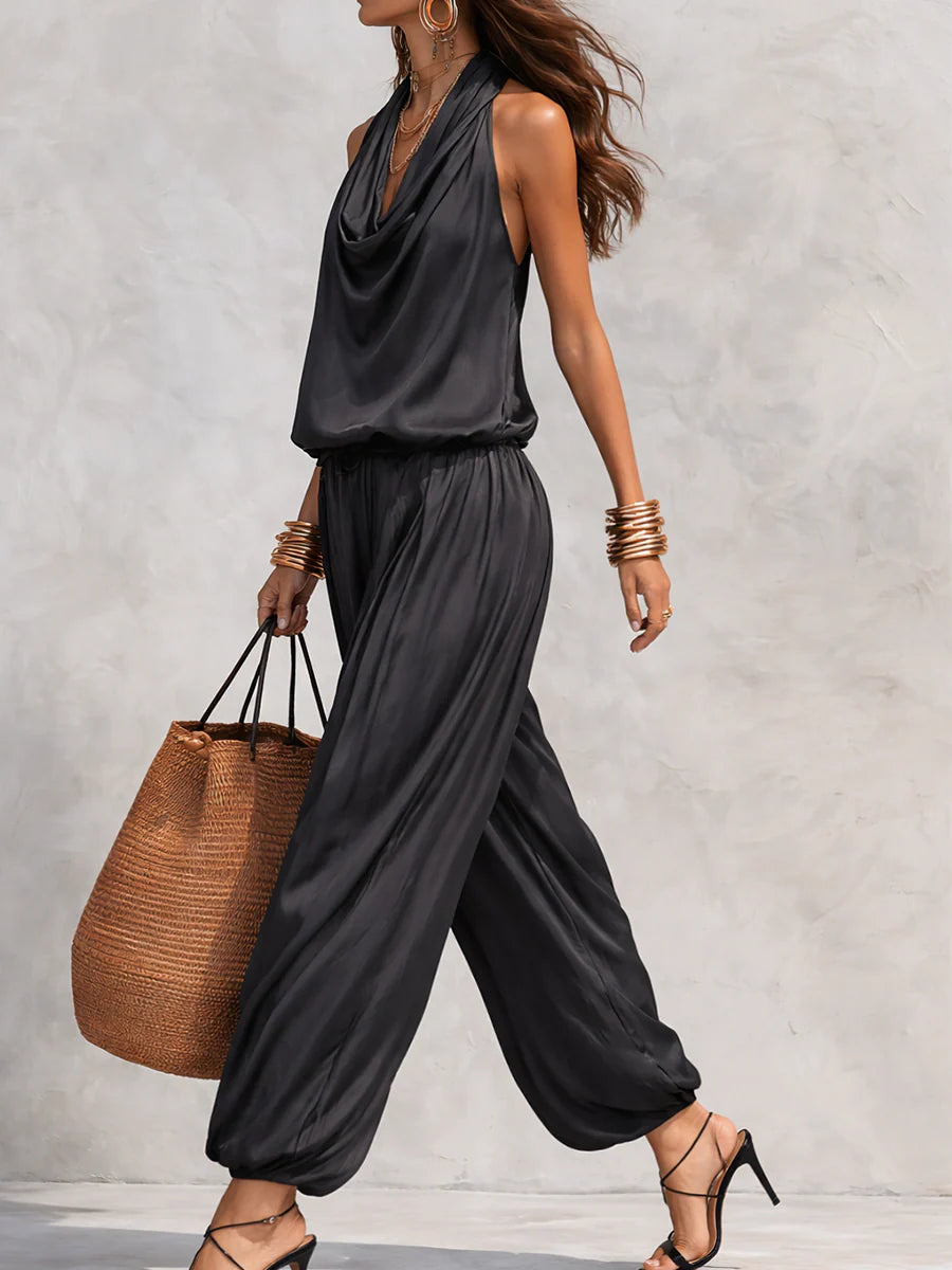 Side view of woman in black two-piece set with draped neckline, carrying a straw bag, outdoor setting.
