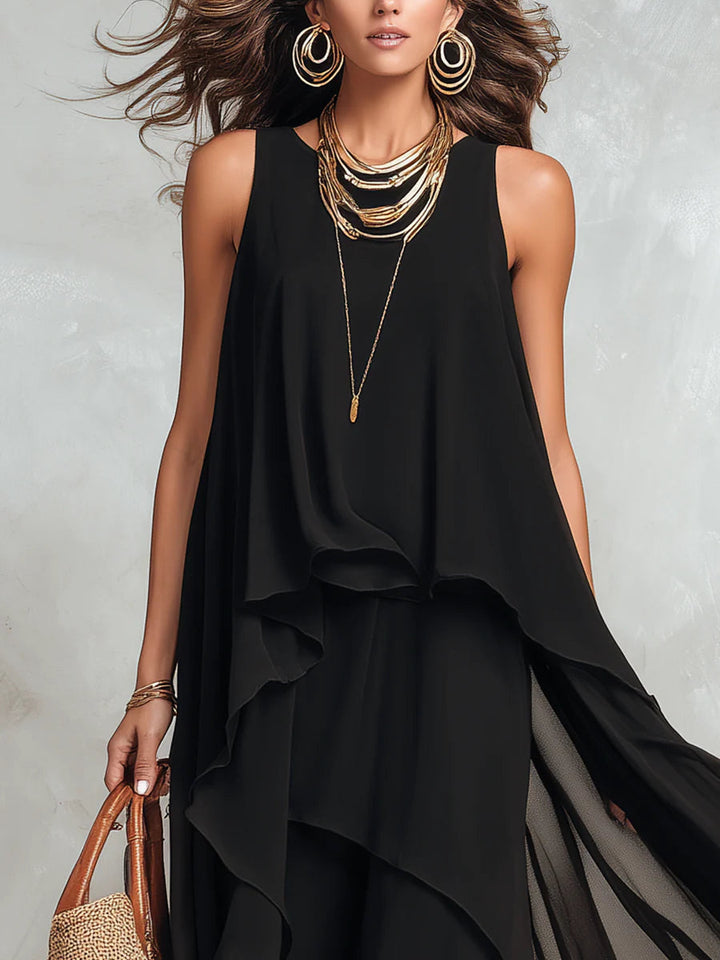 Black maxi dress with layered gold jewelry and straw handbag, showing upper body details. Indoor studio background.