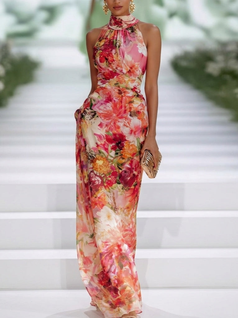 Floral sleeveless maxi dress with a high neckline and vibrant colors, worn by a model on a white staircase runway.