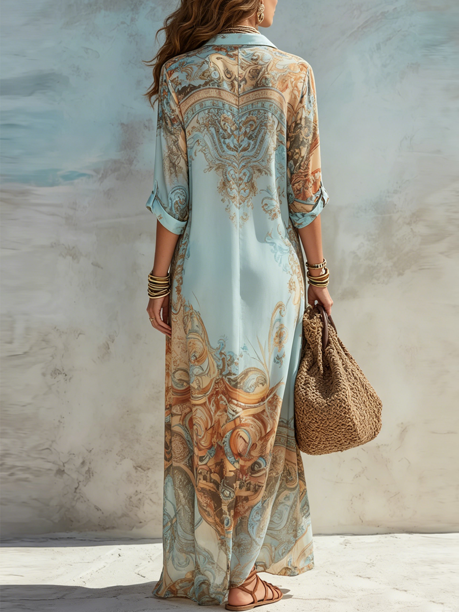 Back view of a flowing maxi dress with intricate blue and brown patterns. The dress is paired with a woven tote and bangles in a textured setting.