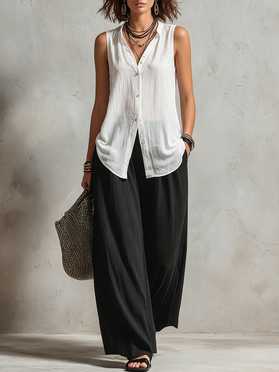 Woman wearing a sleeveless white top and wide black pants with accessories in a minimalist studio setting.