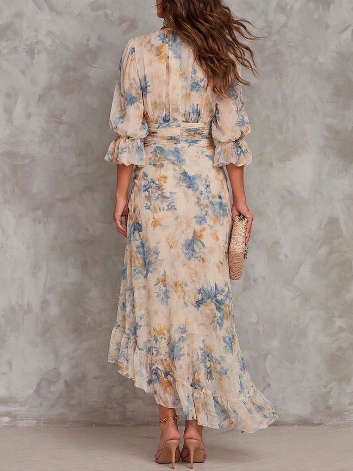 Back view of model wearing a floral maxi dress with ruffled sleeves, holding a clutch against a textured background.
