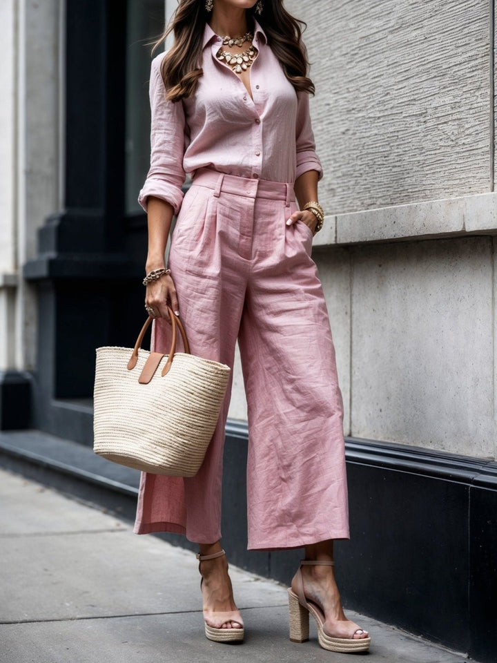 Elegant pink shirt and capri set, paired with nude heels and straw bag, in urban setting.