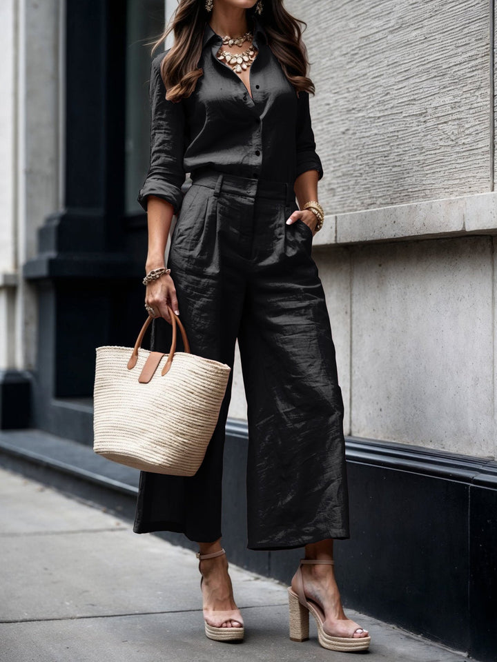 Sophisticated black shirt and capri set, complemented by nude heels and straw bag, on city street.