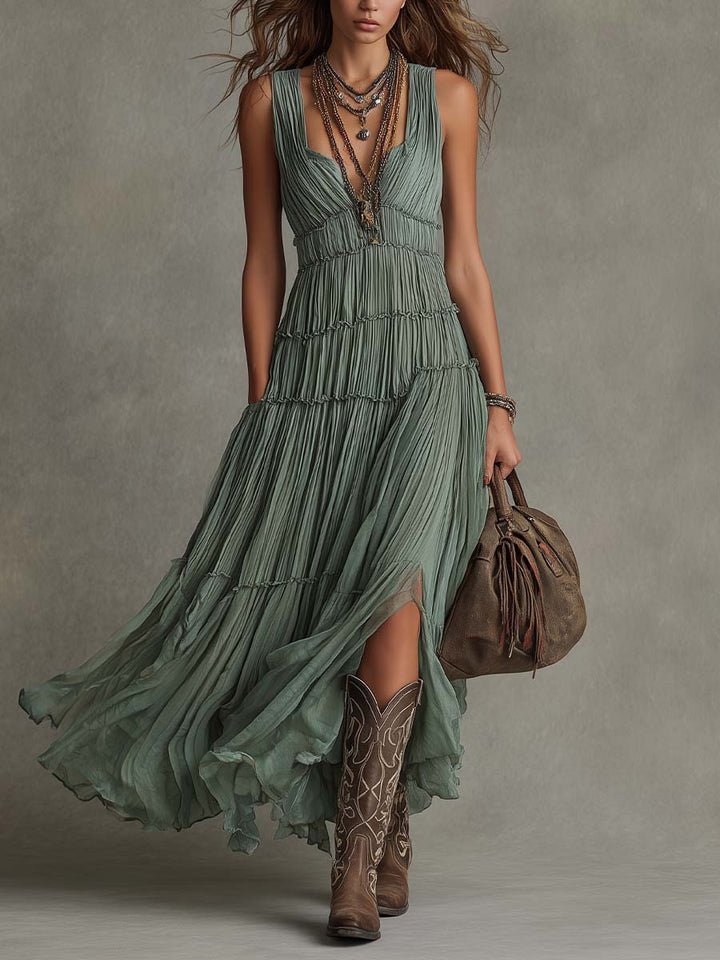 Woman in a flowing green maxi dress with cowboy boots, holding a brown bag. Studio background.