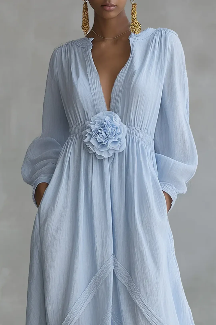Close-up of light blue maxi dress featuring a floral design at the waist, long sleeves, in a neutral studio background.