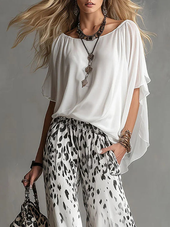 Close-up of woman in a flowing white top, leopard print pants, accessorized with jewelry in a studio setting.