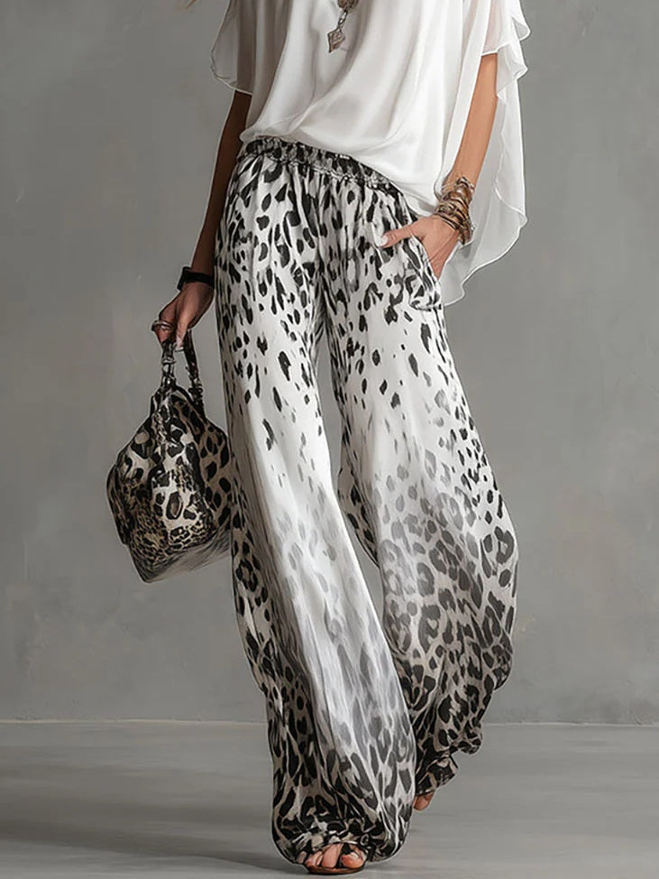 Close-up of leopard print pants and matching bag with a flowing white top in a studio setting.