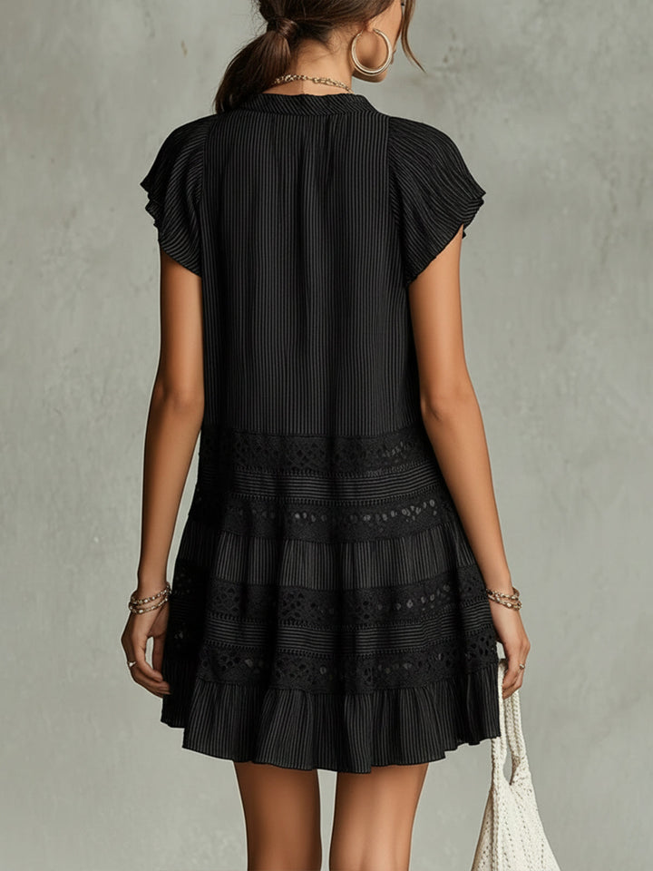 Back view of black striped chiffon mini dress with lace trim and ruffles, modeled in a studio setting.