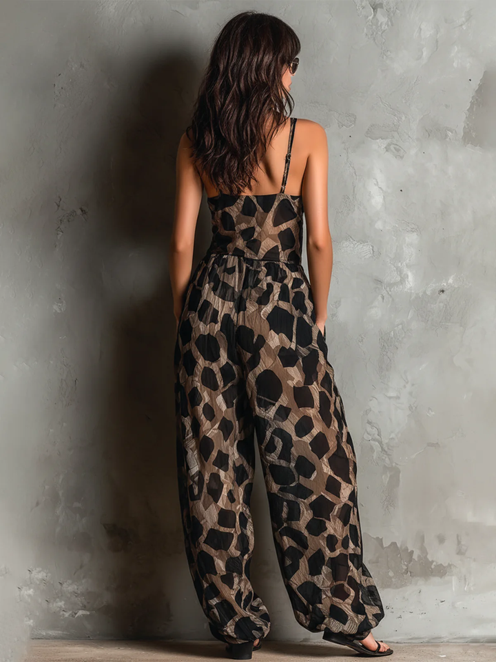 Rear view of black animal print halter-neck chiffon jumpsuit with wide legs in a textured studio.