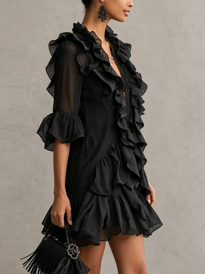 Side view of a woman in a black mini dress with ruffles and lace, holding a fringed handbag in a studio setting.