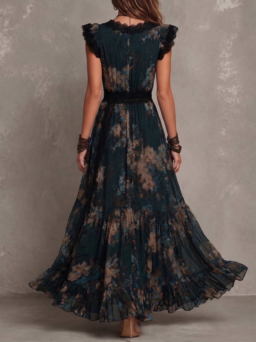 Back view of dark floral maxi dress with black lace accents and tiered ruffles, model standing in studio against gray wall.