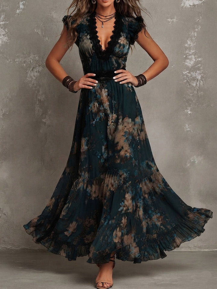 Maxi dress with dark floral pattern and black lace detail, model standing hands on hips in a studio with gray textured walls.