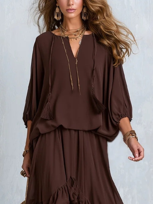 Close-up of brown chiffon top with tassel drawstring, paired with a layered skirt, worn by a woman, light background.